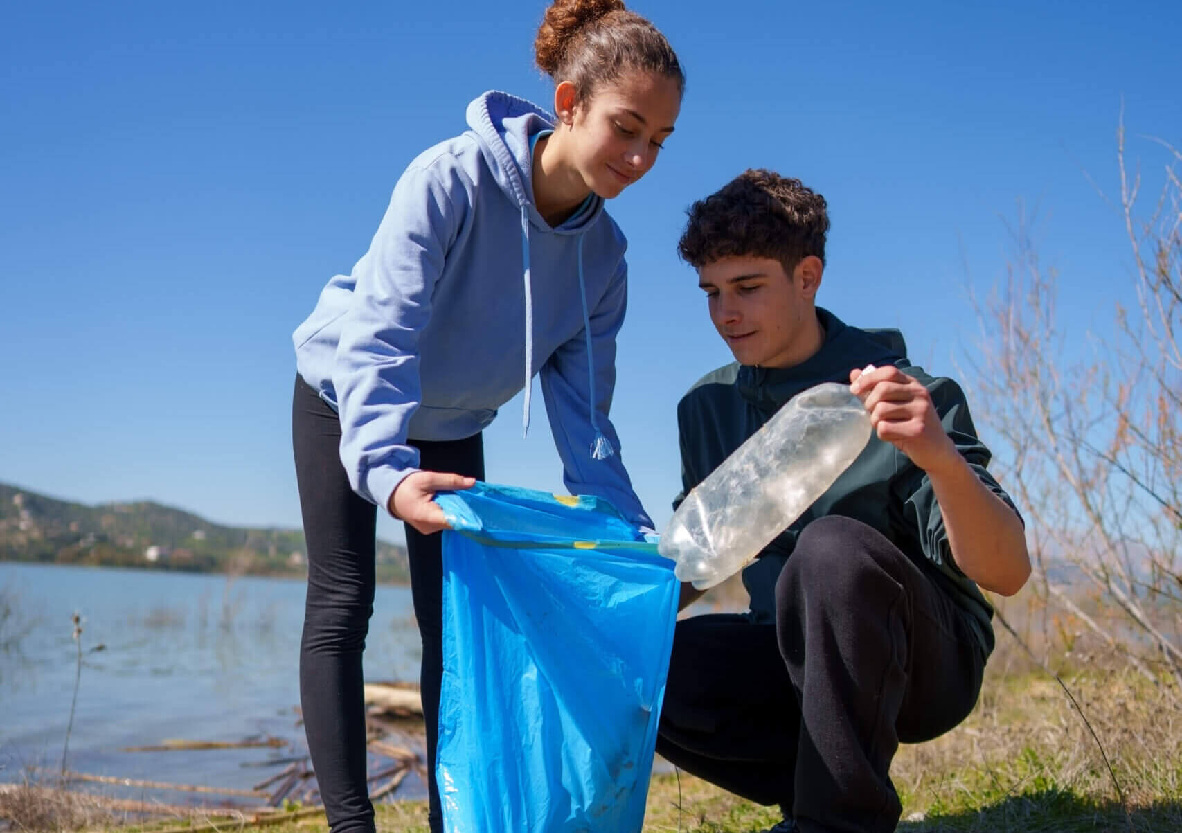 Zwei Jugendliche sammeln Plastikmüll am Seeufer ein