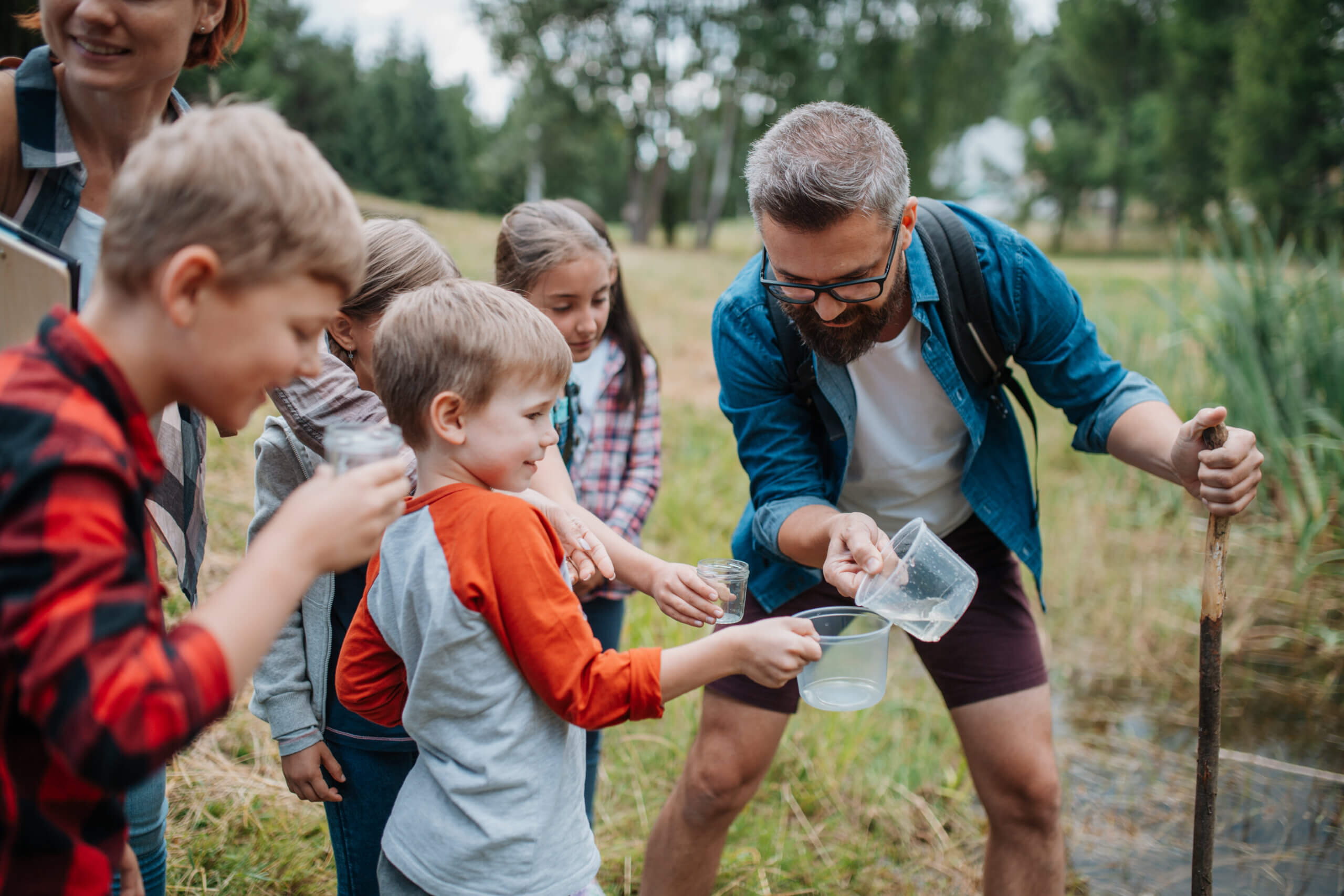 Kinder untersuchen gemeinsam mit einem Betreuer Wasserproben am Gewässer